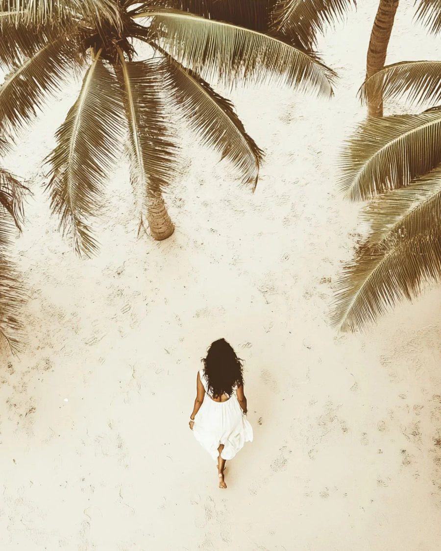 Woman in white dress walking barefoot on sandy beach under palm trees, tropical summer scene