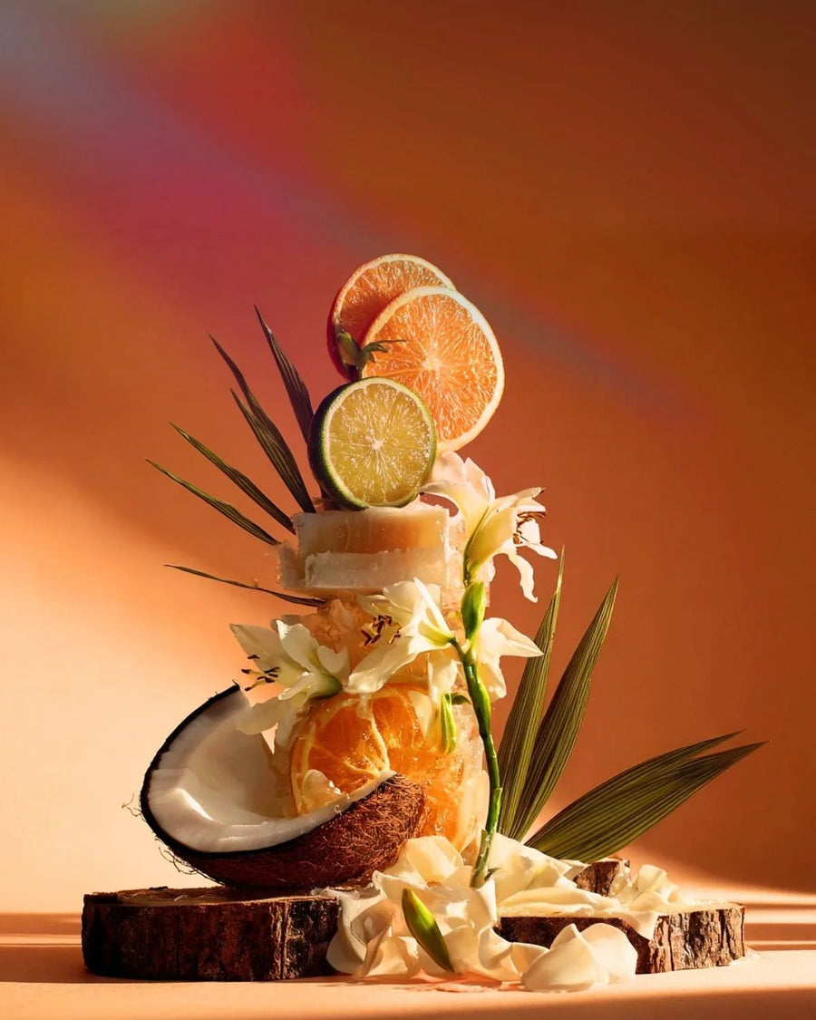 Candle making supplies with coconut, orange, lime, flowers and wood slices on orange background