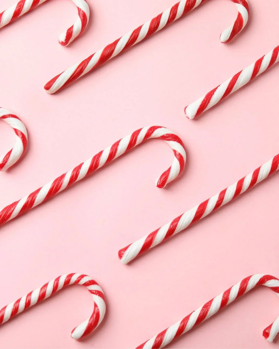 Red and white candy canes arranged on a pastel pink background, festive candy pattern