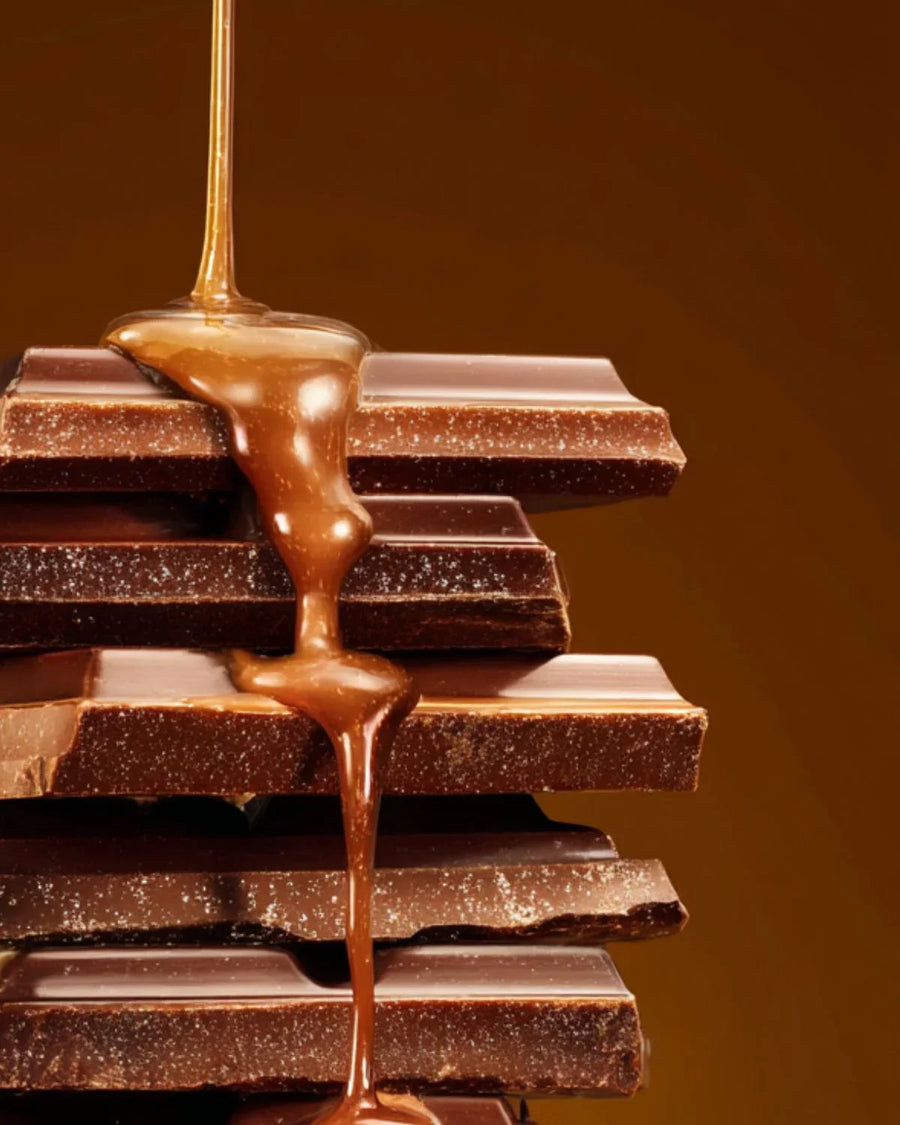 Caramel sauce drizzling over stacked chocolate bars, close-up on brown background.