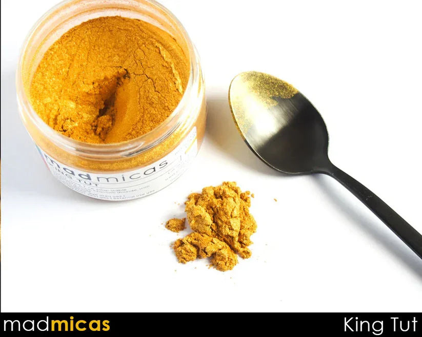 Jar of gold mica powder with a black spoon and gold pigment for soap and candle making.
