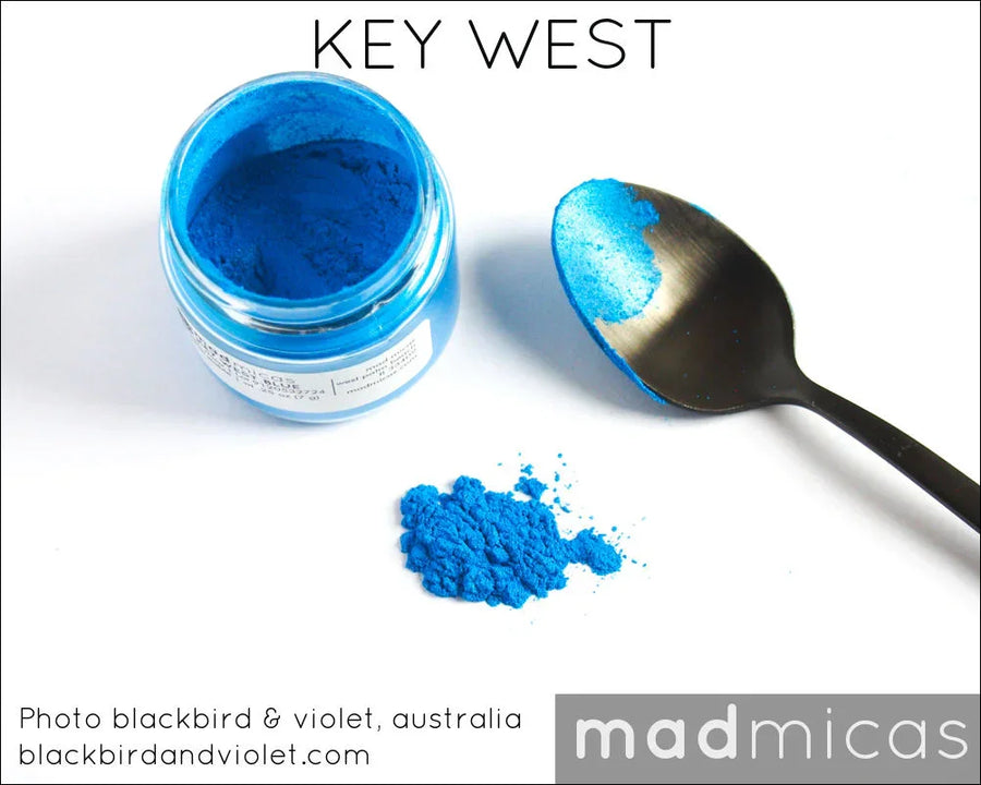 Open jar of vibrant blue mica powder with spoon and spilled pigment, ideal for candle or soap making.