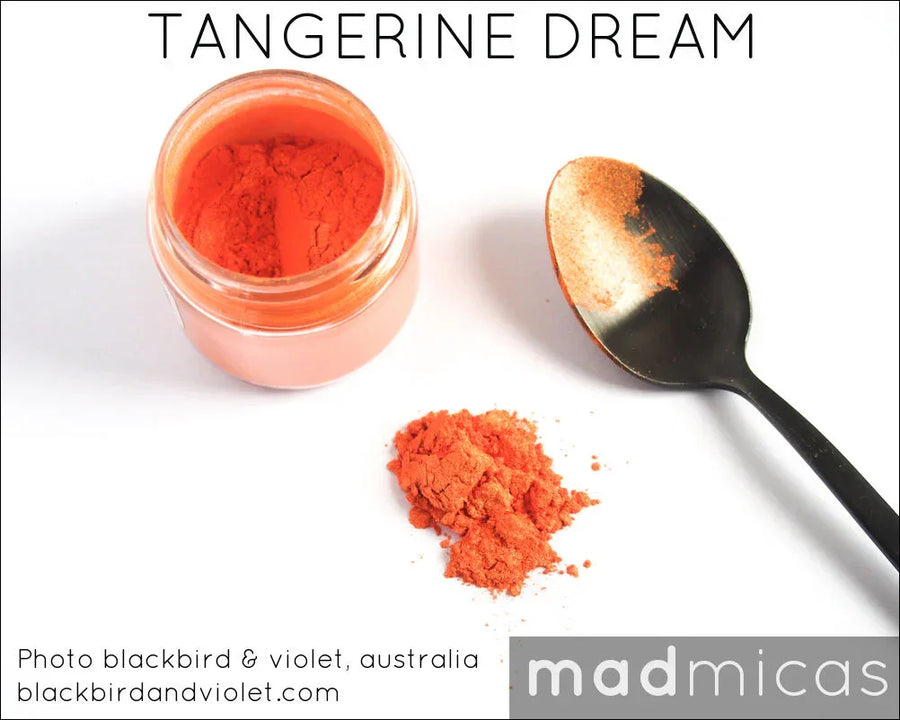 Bright orange mica powder in a clear jar with spoon and loose powder for soap or candle making.