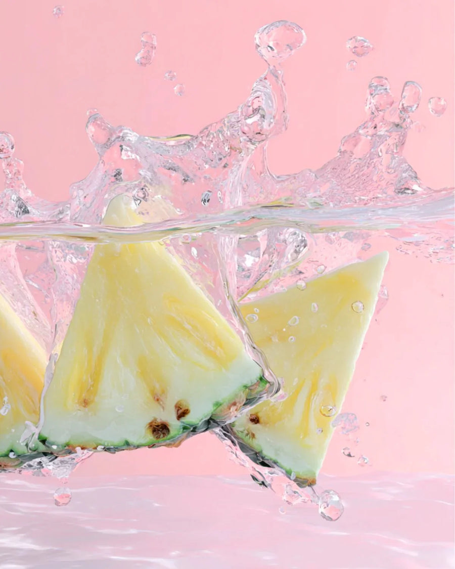 Fresh pineapple slices splashing in clear water on a pink background