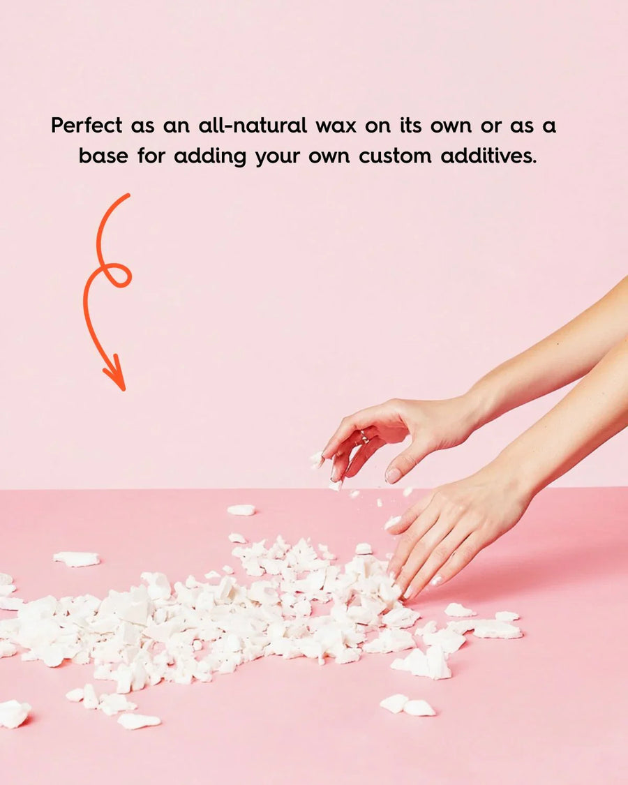 Hands breaking up natural wax flakes for candle making on a pink surface
