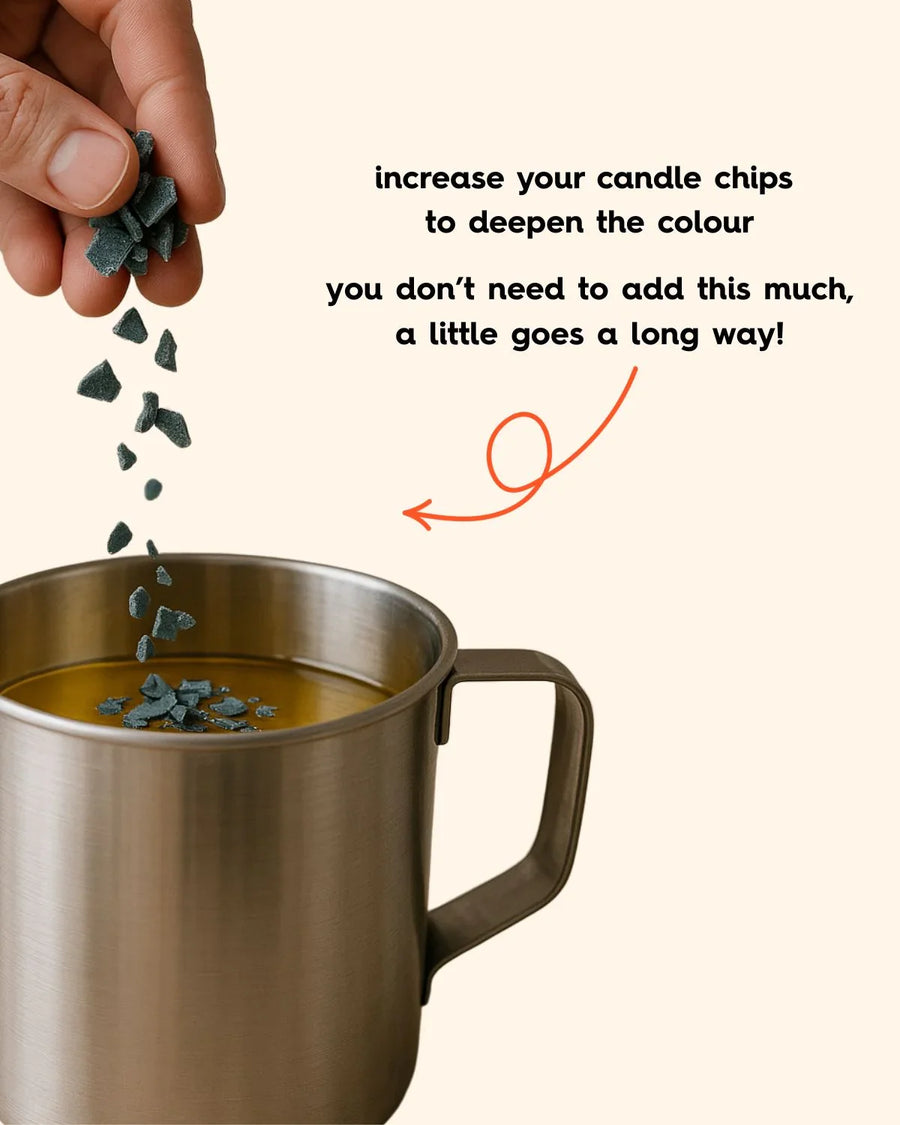 Hand adding candle color chips to melted wax in a stainless steel pouring jug for candle making.
