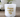 White glass candle with gold 'happy mother's day' text on wooden table, flowers in background
