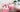 Pink whipped candles in glass jars with white and red decorative topping on a wooden surface