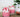 Pink whipped candles in glass jars with white and red decorative topping on a wooden surface