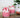 Pink whipped candles in glass jars with white and red decorative topping on a wooden surface