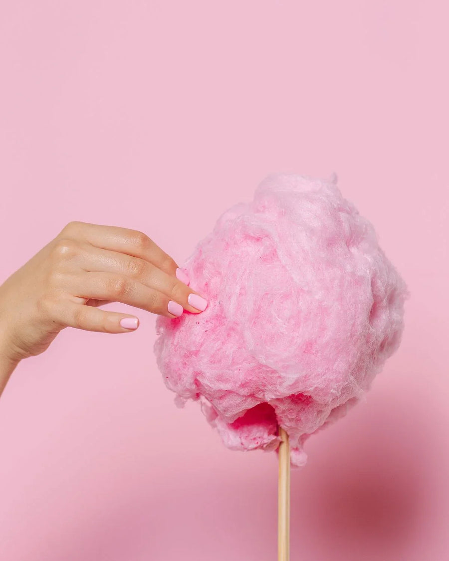 Hand holding pink cotton candy on stick against pastel pink background