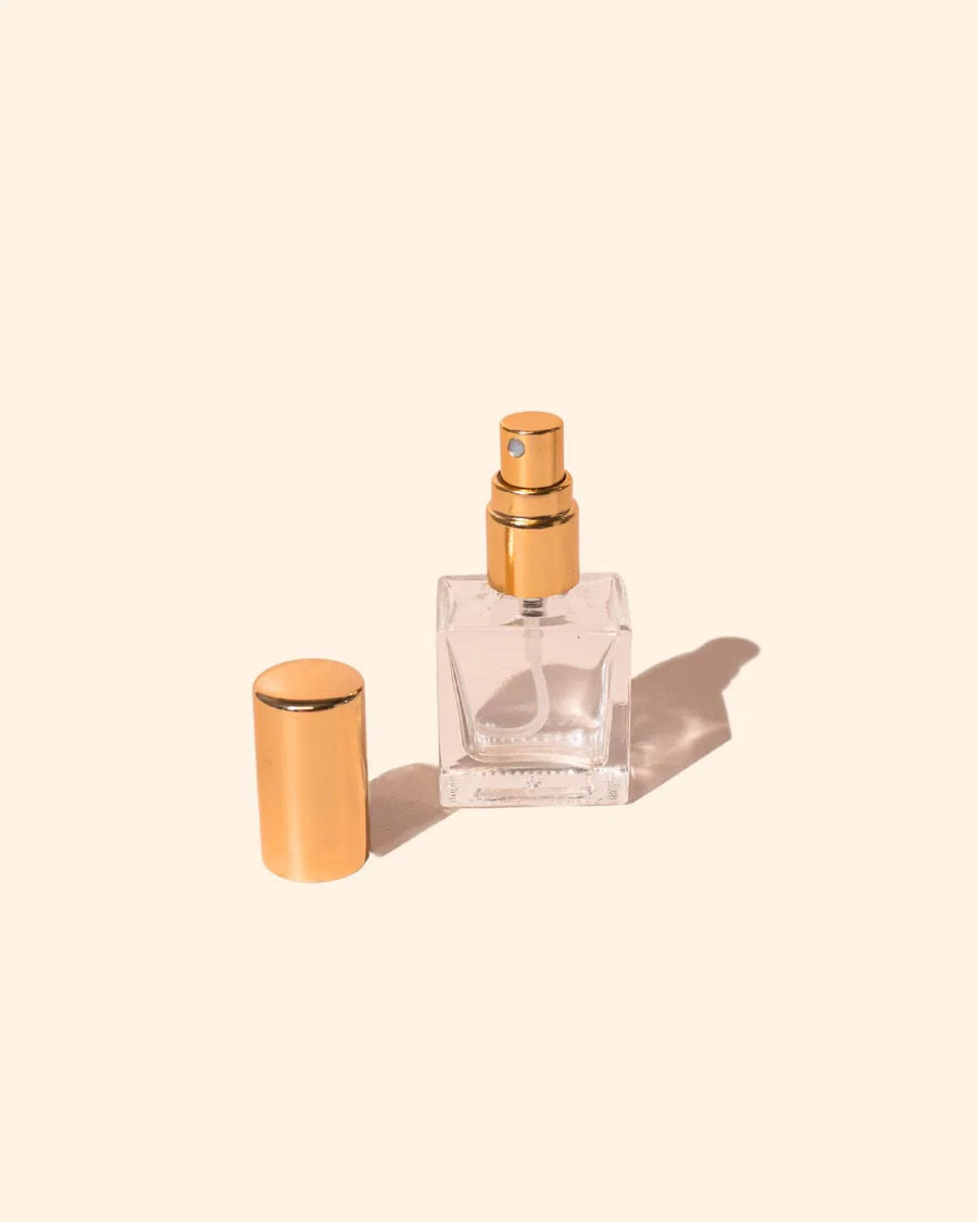 10ml clear glass perfume bottle with gold atomiser and lid on a neutral background