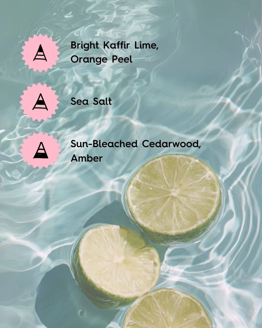 Fresh lime halves float in clear blue water with text listing candle scent notes: kaffir lime, orange peel, sea salt, cedarwood, amber.
