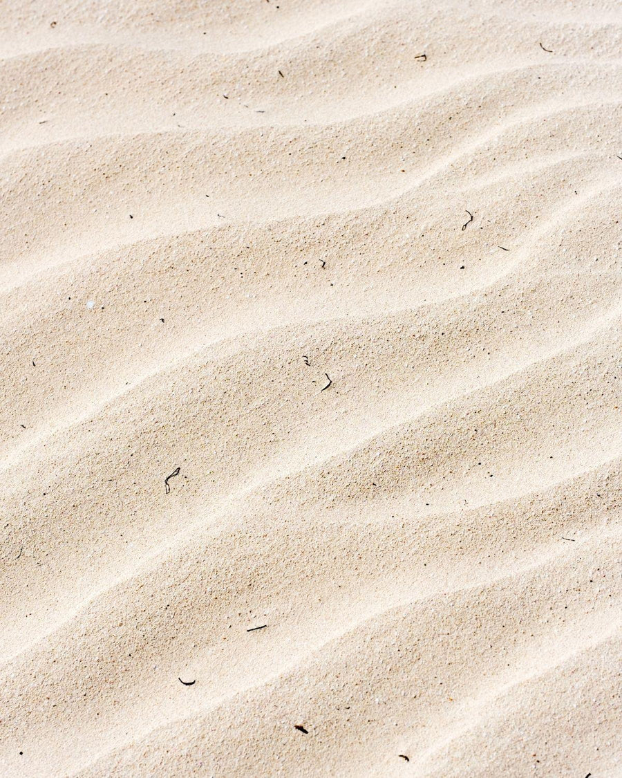 Close-up of textured sand with natural wave-like patterns and small debris.