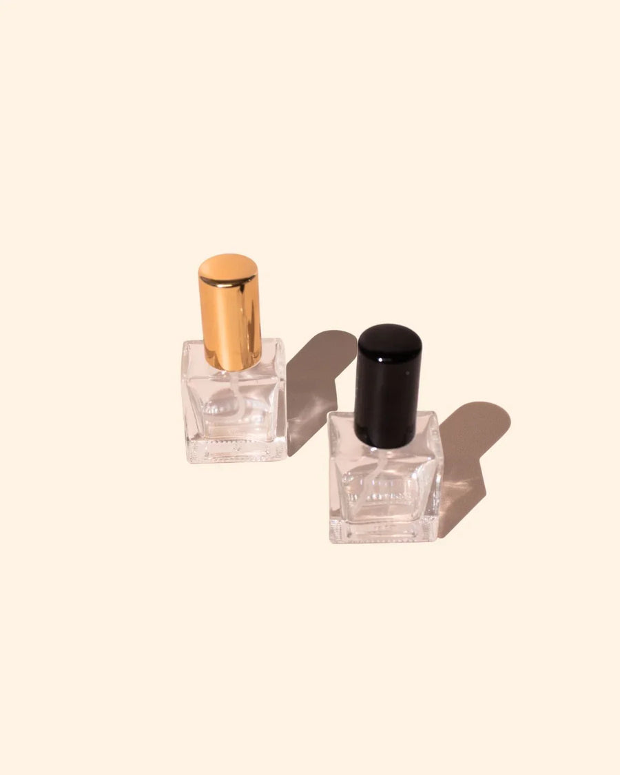 Two 10ml rectangular glass perfume and cologne bottles with gold and black atomiser caps on a beige background