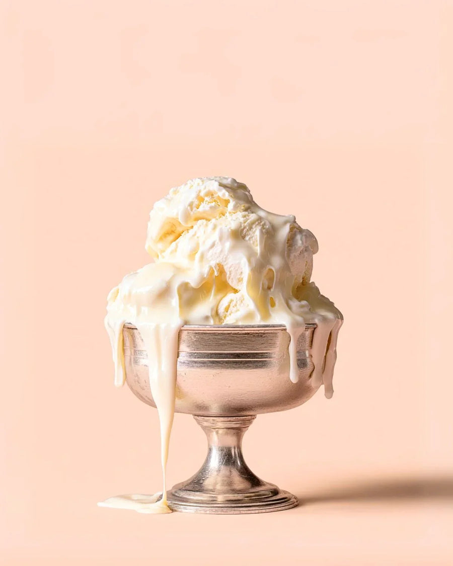 Melting vanilla ice cream scoops in a silver dessert bowl on a peach background
