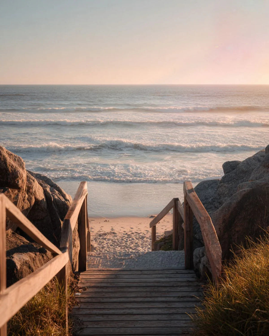Wooden stairs leading to sandy beach with ocean waves at sunset
