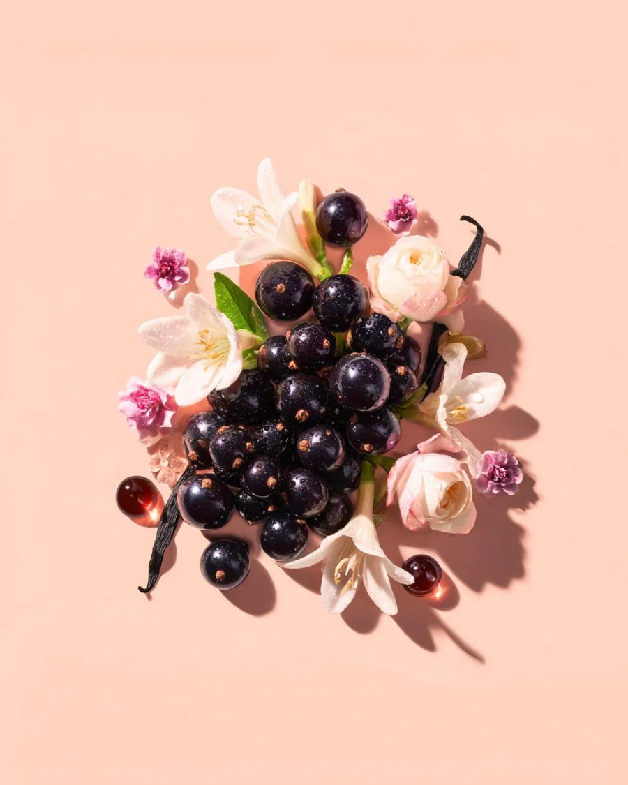 Blackcurrants, vanilla pods, and assorted flowers on a peach background for fragrance oil.