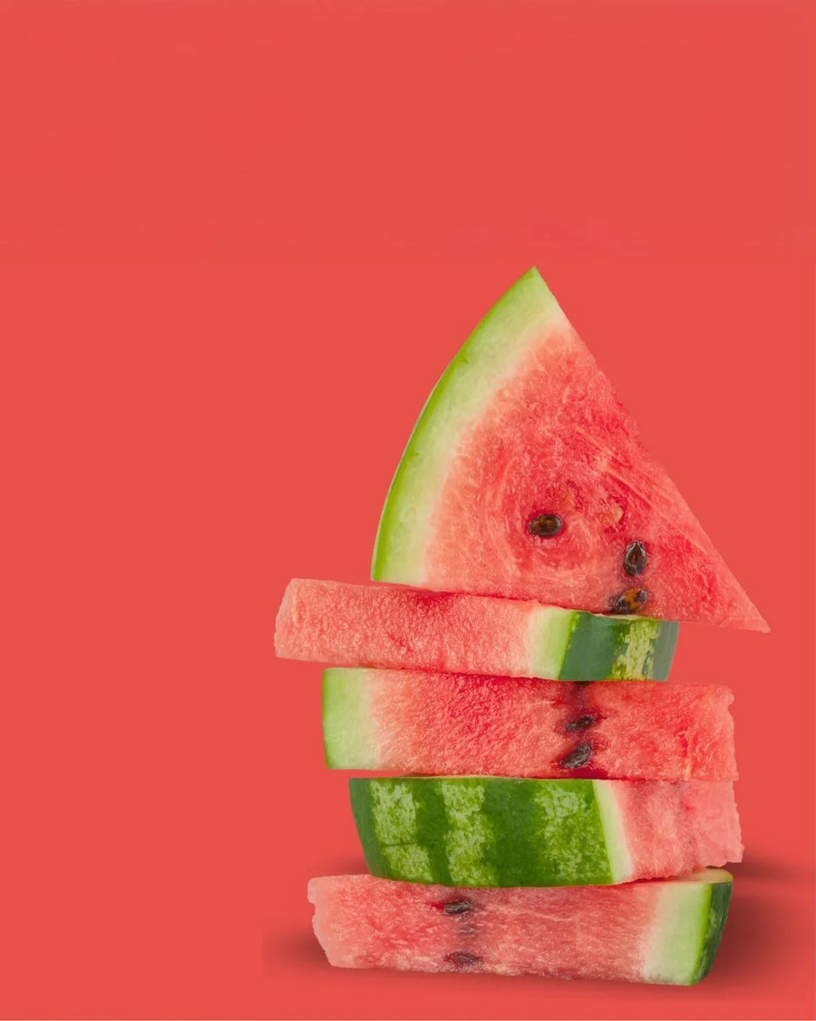 Stacked watermelon slices with green rind and red flesh on a solid coral background