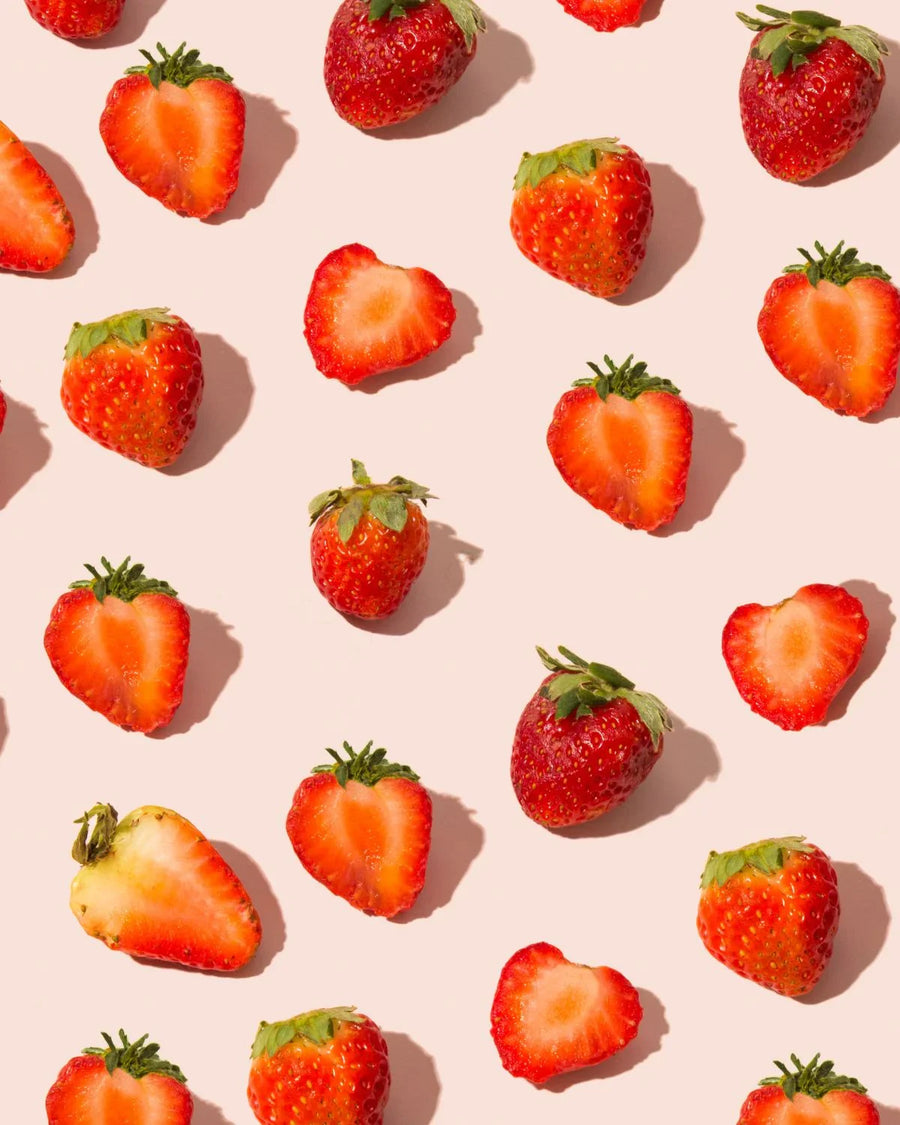 Fresh whole and halved strawberries scattered on a light pink background, vibrant fruit pattern