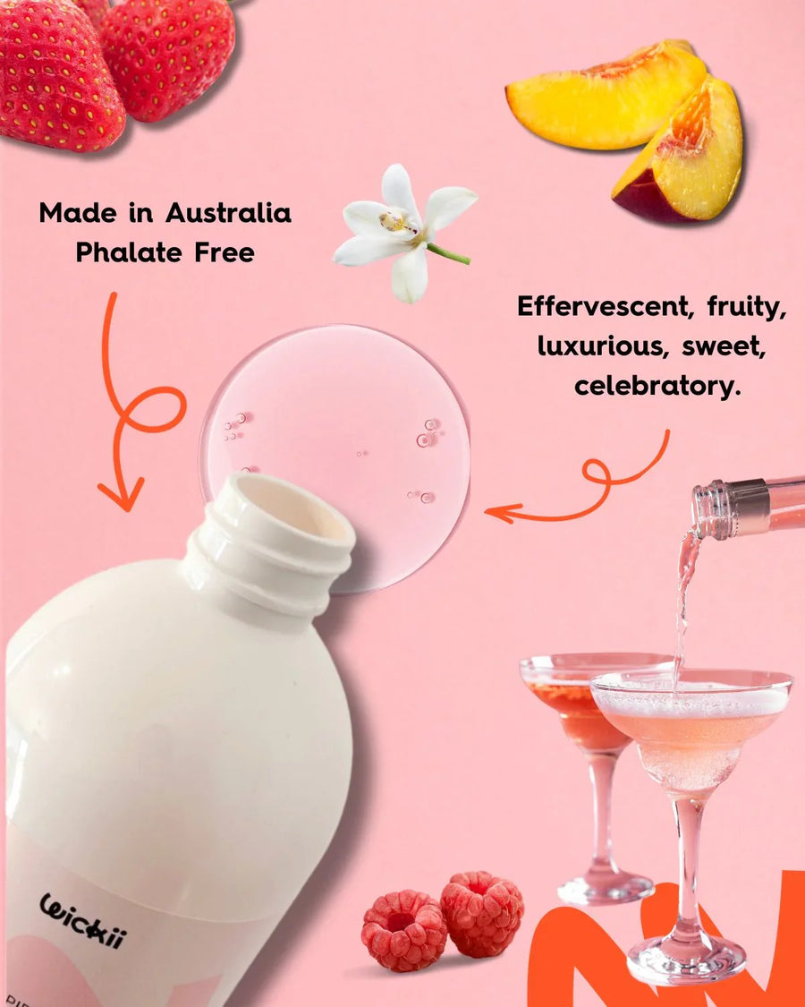 Pink fragrance oil bottle with strawberries, peach slices, raspberries, champagne glasses and floral notes on pink background.