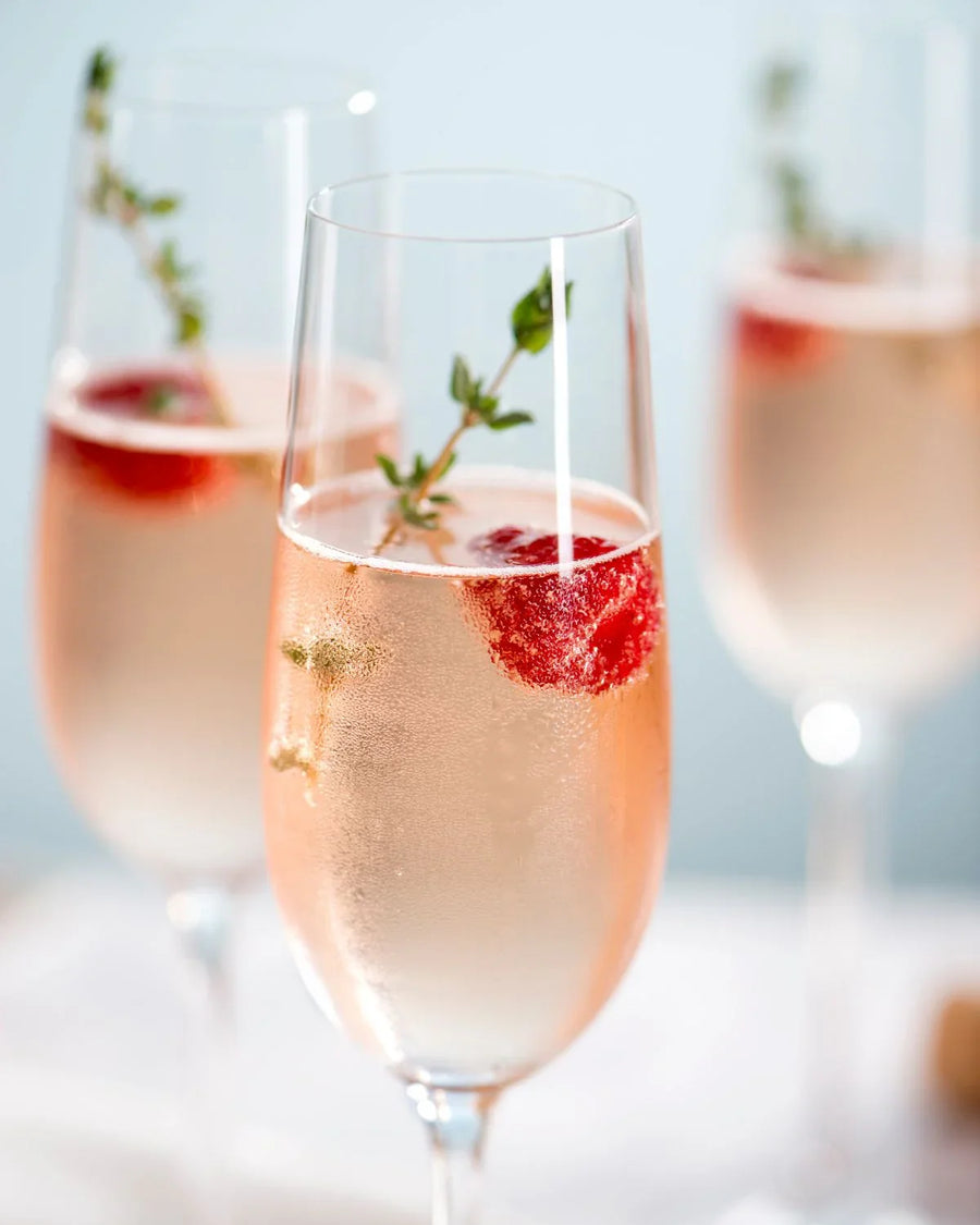 Sparkling rosé in champagne flutes with raspberries and thyme garnish