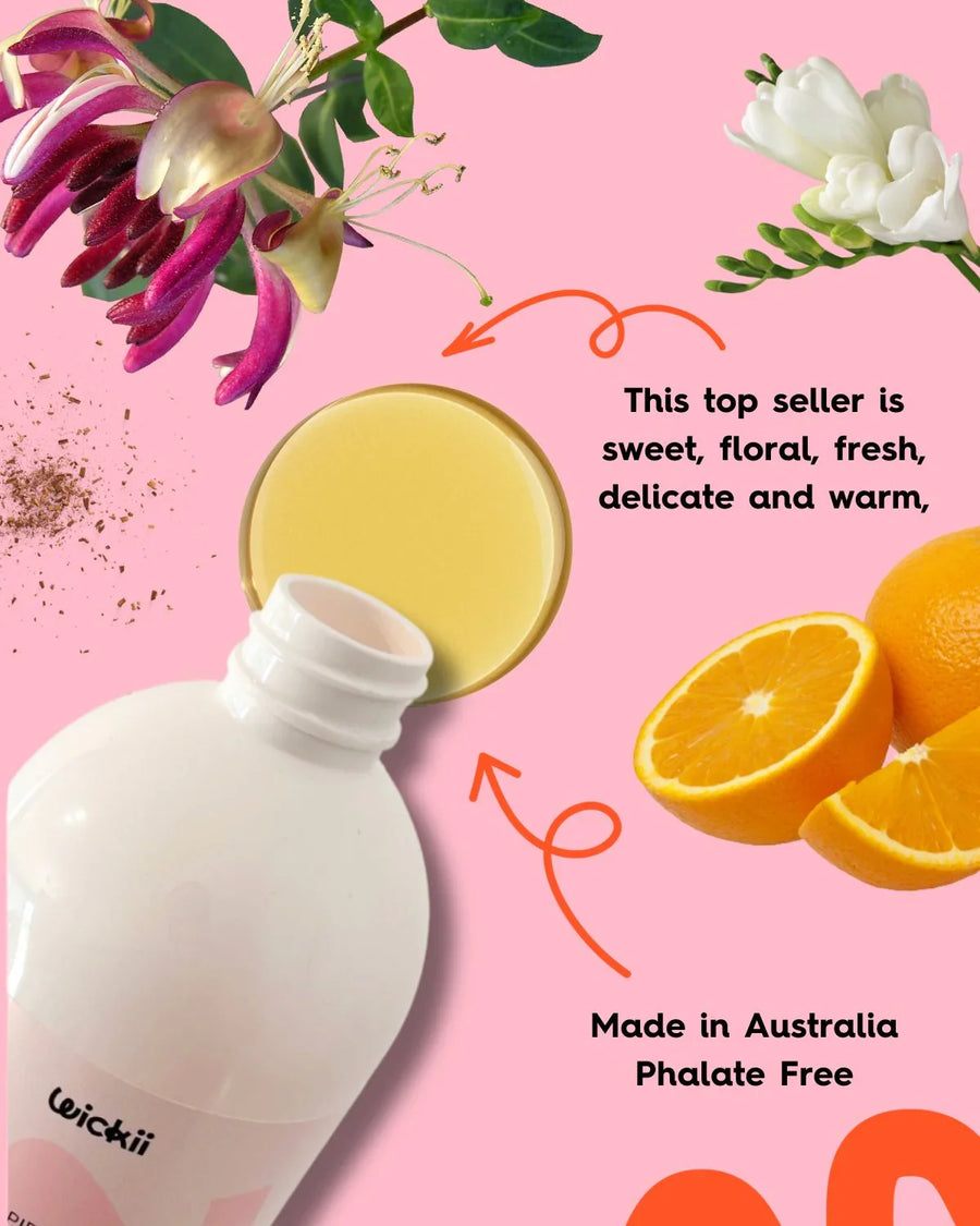 Bottle of fragrance oil with honeysuckle, fresh oranges, and flowers on a pink background