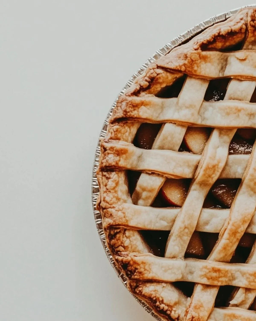 Close-up of a classic lattice-crust pie in a foil tin on a light background.