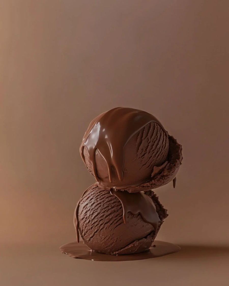 Two scoops of chocolate ice cream with chocolate syrup, stacked on a brown background.