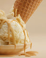 Vanilla ice cream in bowl with caramel sauce and waffle cone on neutral background