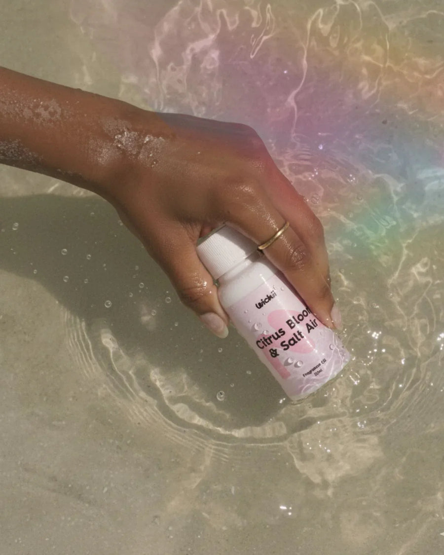 Hand holding Citrus Bloom & Salt Air fragrance oil bottle over water with sunlight reflections