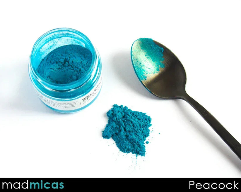 Peacock teal blue mica powder in a jar, with a spoon and powder spill for soap and candle making.