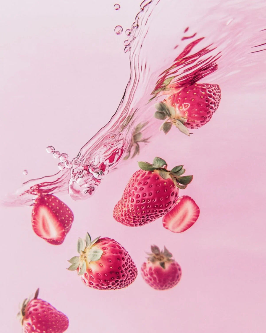 Fresh strawberries splashing in water with pink background, fragrance oil inspiration.