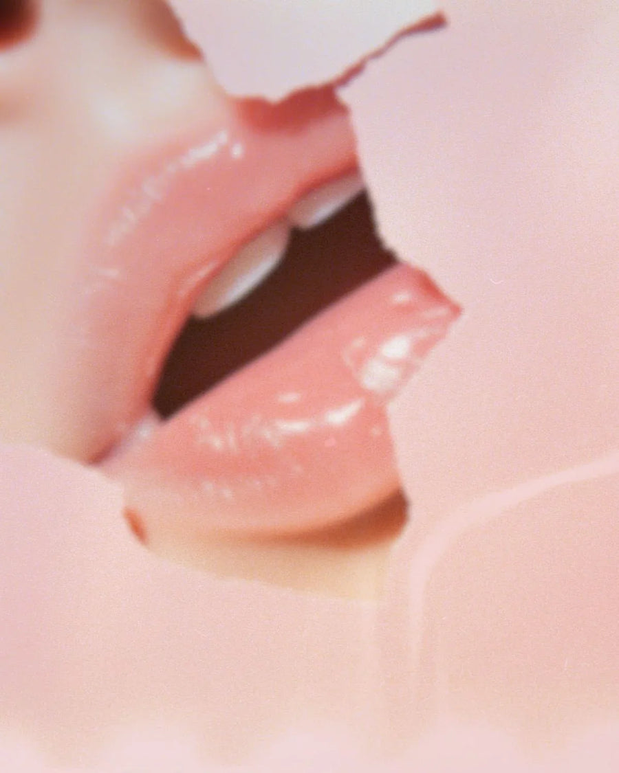 Closeup of glossy pink lips seen through torn pastel paper, soft and artistic focus