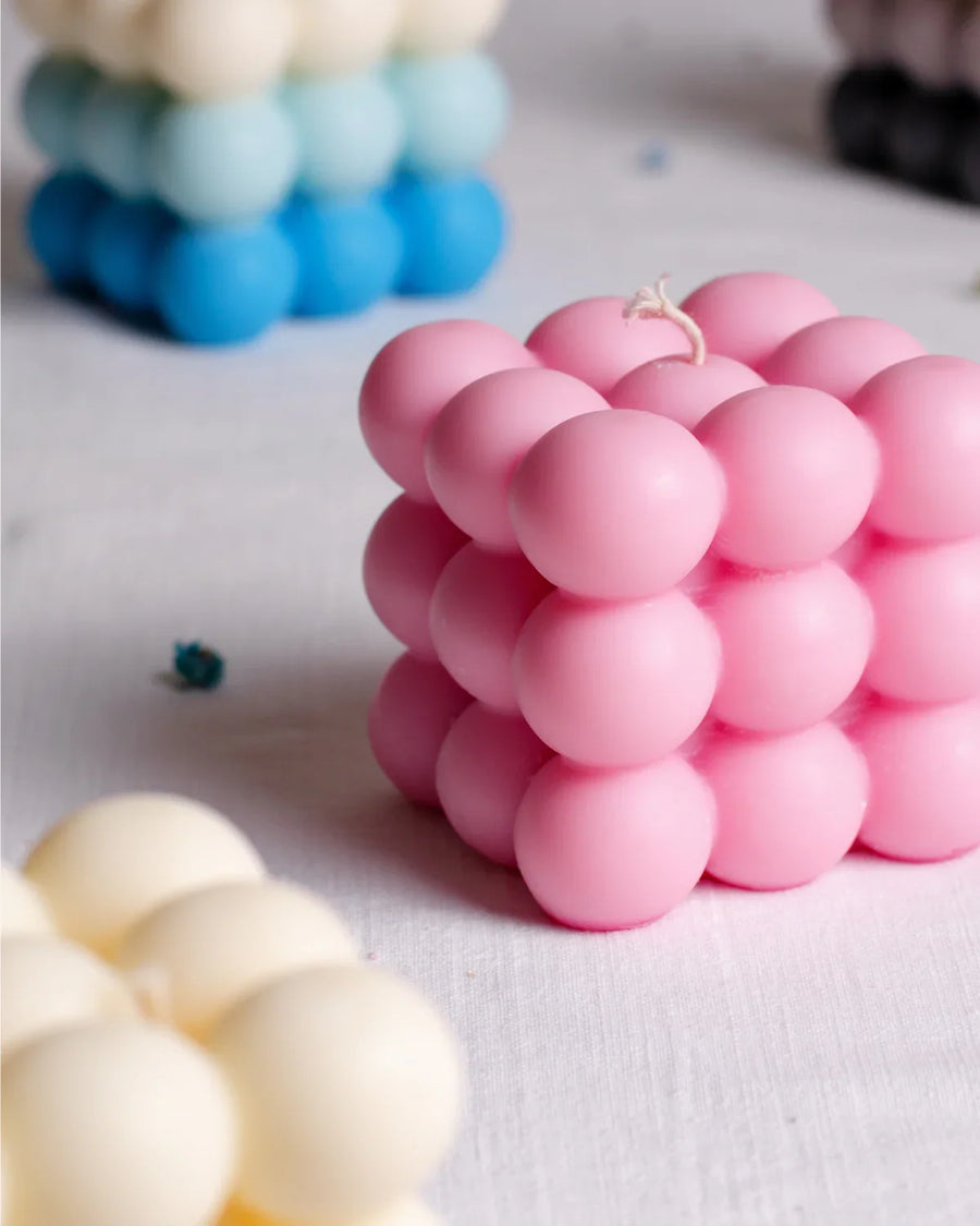 Pink bubble cube candle on white table with colorful bubble candles in background