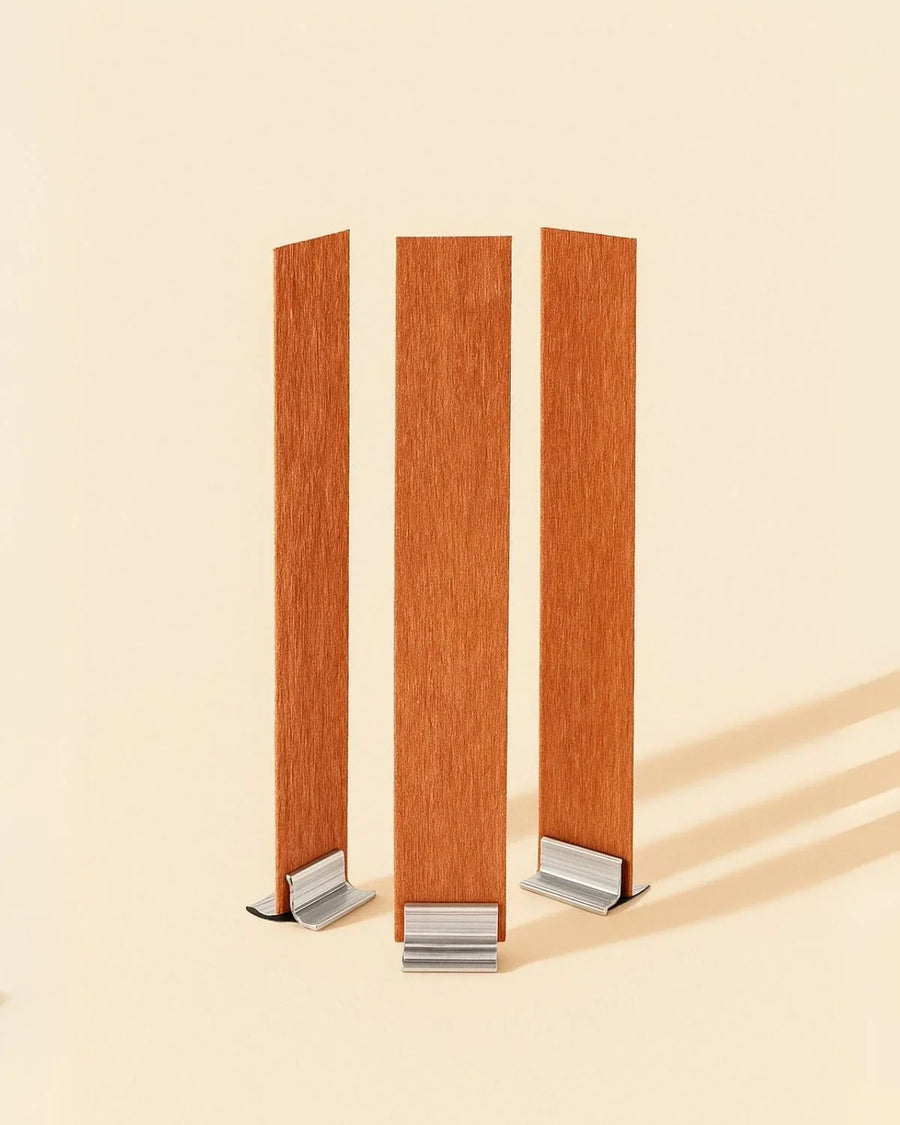 Three wooden candle wicks with metal tabs standing upright on a beige background