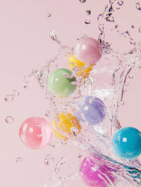 Colorful bubblegum balls splashing in clear water against a light pink background