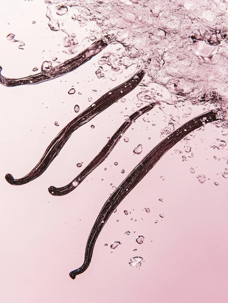Vanilla beans splashing in clear water against a light pink background
